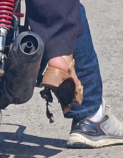 A photo of two feet, belonging to two different people sitting on the same motorbike. One has a sneaker on, the other has a platform shoe with a melted plastic sole, probably from the hot exhaust pipe.