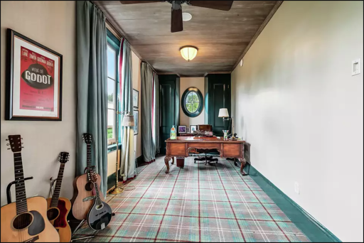 Long office with plaid carpet. On the left wall stands 3 acoustic guitars and a mandolin. Above the instruments is a poster from the Broadway production of "Waiting for Godot" starring Nathan Lane & John Goodman. Green curtains decorate two wall-sized pane windows. At the end of the office is an oval paned window and a handsome carved oak desk. Above it all is a ceiling fan and a domed light fixture above the desk.