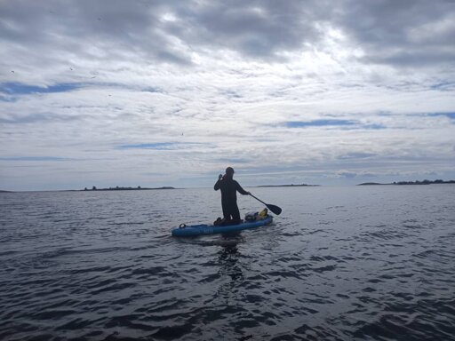 Photo of me on a paddelboard on the open sea with a cloudy sky above and some islands in the distance.