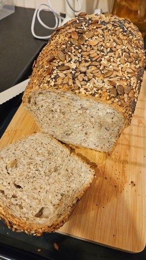 Homemade seeded whole wheat loaf bread. The first slice is on the wood cutting board. 